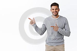 Good-looking charming bearded caucasian guy with short stylish hairstyle, wear grey sweater, pointing left, advertise