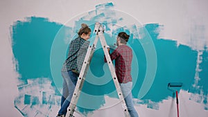 Good looking couple Caucasian painting together the walls at home in a blue colour and discussing at the same time lady