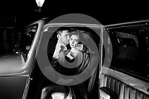 Good looking couple, handsome man in suit, beatiful woman in red dress, embrace passionately in vintage car