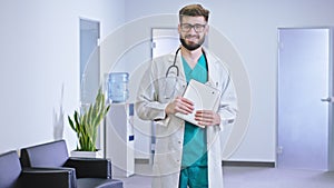 Good looking doctor man standing in front of the camera in the modern hospital corridor holding his electronic tablet