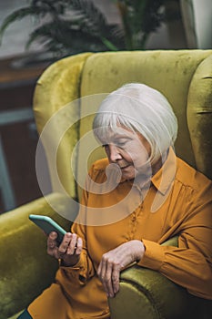 Good-looking elderly lady in yellow looking at her phone