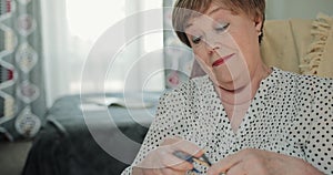 Good looking elderly woman holding knitting pins while sitting on chair. Mature beautiful lady spending free time and