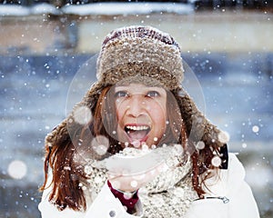 Good looking Girl in Winter Clothing blows white Snow and smiles in front of a wooden barn with lots of snow falling from the sky photo