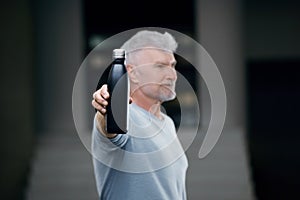 Good looking gray haired senior man in white shirt with water bottle. Sport and health care concept