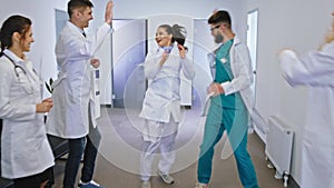 Good looking group of doctors and nurses dancing in front of the camera in a modern hospital corridor. 4k