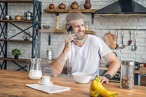 Good looking handsome bearded man is sitting in the kitchen having breakfast cereals and milk, coffee and bananas. reading morning