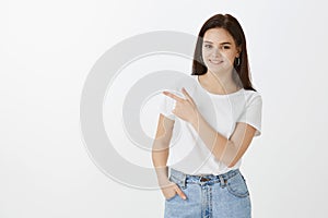 Good-looking happy and stylish caucasian urban woman in jeans and t-shirt, holding hand in pocket while pointing at