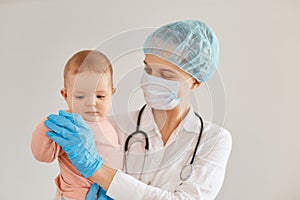 Good looking kind young adult female pediatrist wearing medical uniform, being photographed with cute little patient, holding