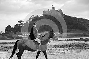 Good Looking Male Horse Rider riding horse on beach in traditional riding clothing with St Michael`s Mount in background