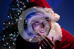 Handsome male santa smiling and holding lights in his hand with christmas tree in background