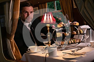 Good looking man in suit enjoying afternoon tea in vintage train carriage