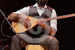 Good-looking man with a thick black beard, hands of musician playing a typical stringed instrument on stage, the tembur