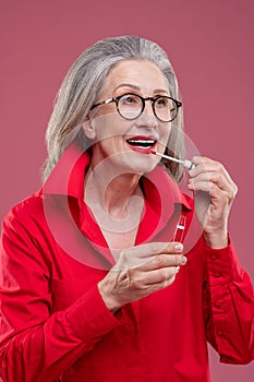 Good-looking mid aged woman putting lip gloss on her lips