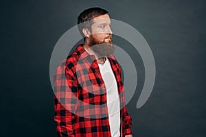 Good-looking modern hipster guy with beard in red checkered shirt, standing half-turned with spaced-out casual expression, looking