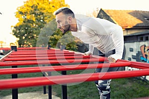 Good looking muscular young man working out on the horizontal ladder under the sky, outdoors workout
