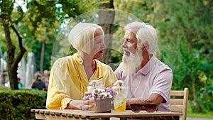 Good looking old man and his beautiful wife old woman have a perfect time together in the middle of the park at the cafe