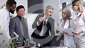 Good-looking respectable gray-haired male head doctor telling to his mixed race doctors-colleagues about chemical