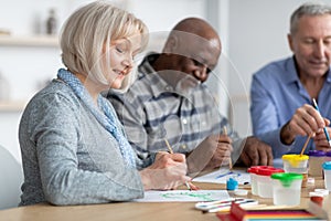 Good-looking senior lady enjoying painting activity with her friends