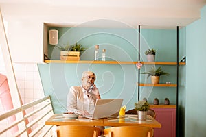 Good looking senior woman working on laptop, drinking orange juice and having a healthy breakfast in cafeteria