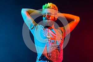 Good looking serious guy with beard wearing denim overalls looking away with confident facial expression, keeping hands raised