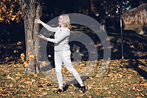 Good-looking smiling middle-aged woman with long wavy fair hair in grey roll-neck sweater throw up yellow maple leaves.