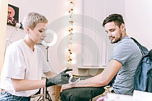 Good-looking tattoo master with boyish haircut wiping off area of bare skin