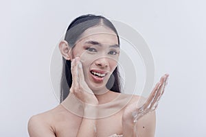 A good-looking transwoman freshens up by washing her face with hydrating and moisturizing facial wash. Studio shot isolated on a