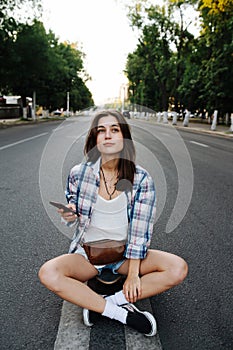 Good looking woman sitting in the middle of an empty city road, phone in hand