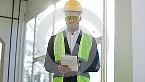 Good looking young architect man with safety equipment at construction site using digital tablet to analysing the plan