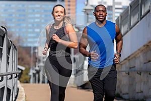 A good looking young athletic couple running through the city in urban lifestyle active sport portrait, buildings in background