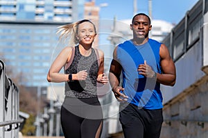 A good looking young athletic couple running through the city in urban lifestyle active sport portrait, buildings in background