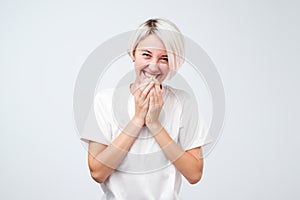 Good looking young female with dyed hair wearing white t-shirt giggles joyfully, covers mouth as tries stop laughing