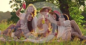 Good looking young friends clinking with glass bottles while having picnic together. Millennial happy people smiling