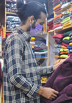 A good looking young guy wearing face mask looking at clothes to buy in clothing store during coronavirus pandemic
