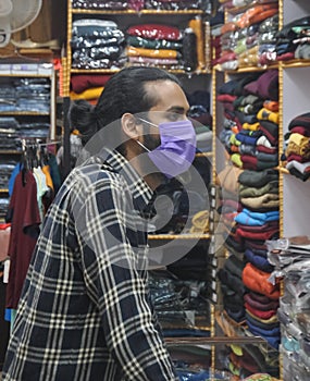 A good looking young guy wearing face mask looking at clothes to buy in clothing store during coronavirus pandemic