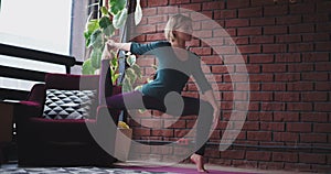 Good looking young lady in a sportswear at home using a sofa to make a hard exercise using yoga Tehnic to stretching the
