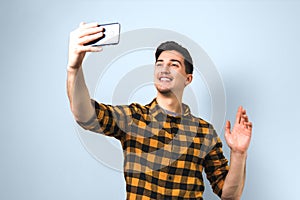 Good looking young man in casual yellow shirt video-chatting via smartphone isolated against light blue background