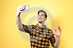 Good looking young man in casual yellow shirt video-chatting via smartphone isolated against yellow background