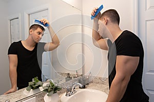 Good Looking Young Man Combing and Looking at His Hair, Beard, and Face in His Home Bathroom Mirror in the Morning Getting Ready f