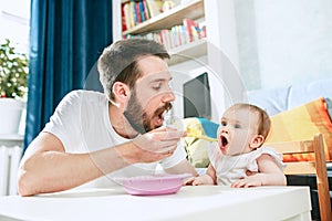 Good looking young man eating breakfast and feeding her baby girl at home