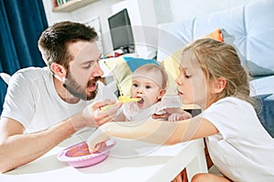 Good looking young man eating breakfast and feeding her baby girl at home