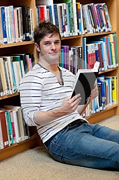 Good-looking young man holding a book on the floor