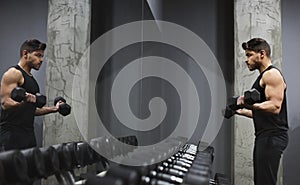 Good looking young man lifting dumbbells in front of mirror