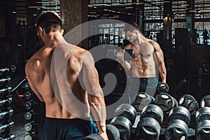 Good looking young man lifting dumbbells and working on his biceps in front of the mirror looking on his biceps