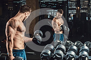 Good looking young man lifting dumbbells and working on his biceps in front of a mirror looking on his biceps