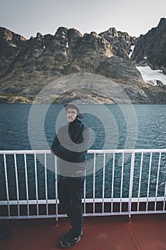 Good looking young man looking forward and smiling while standing on the deck of a ship in the Arctic. On Board Sarfaq