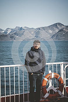 Good looking young man looking forward and smiling while standing on the deck of a ship in the Arctic. On Board Sarfaq