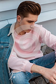 Good-looking young man with trendy hairstyle in fashionable blue youth jeans clothes from new summer collection rest on street