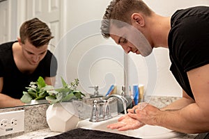 Good Looking Young Man Washing Hands and Face in Home Bathroom Mirror and Sink Getting Clean and Groomed During Morning Routine