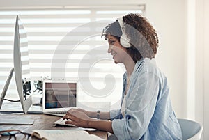 This good mood was sponsored by music. an attractive young woman sitting alone at home and using her computer while